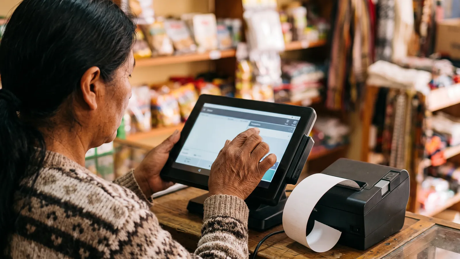 Manos de una comerciante en la pantalla del POS mientras la impresora saca el comprobante